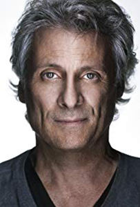 Close-up portrait of a middle-aged man with wavy graying hair looking directly at the camera.