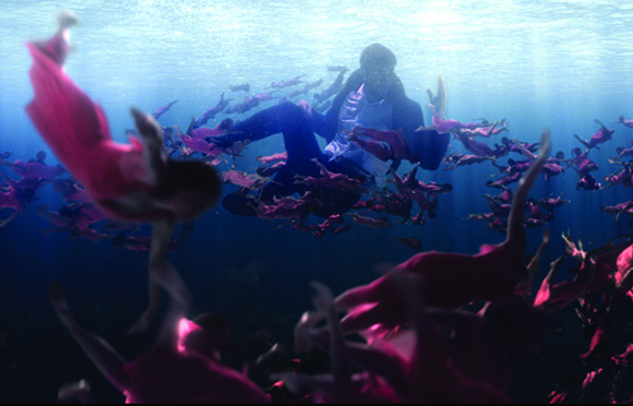 A man floats in deep blue water surrounded by many people wearing pink clothing.