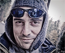 Close-up of a man wearing dark sunglasses and a grey knit hood outdoors.