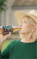 A blonde woman in a straw hat and green sweater drinks from a bottle of iced tea.