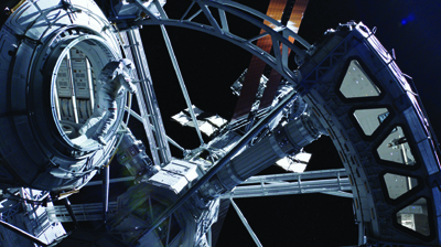 An astronaut in a white spacesuit floats near a large circular hatch on a complex space station structure.