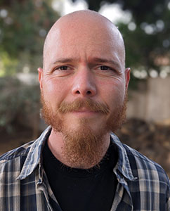 A bald man with a reddish-brown beard and mustache wearing a plaid shirt.