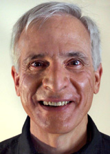 Close-up headshot of a smiling man with graying hair and a black collared shirt.