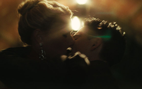 A close-up of a man and a woman kissing in a dimly lit setting with soft bokeh lights.