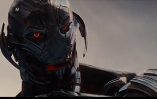 A metallic humanoid robot head with glowing red eyes and dark plating against a pale sky.