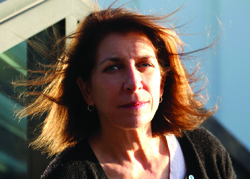 A woman with reddish-brown hair blowing in the wind, looking forward in sunlight.