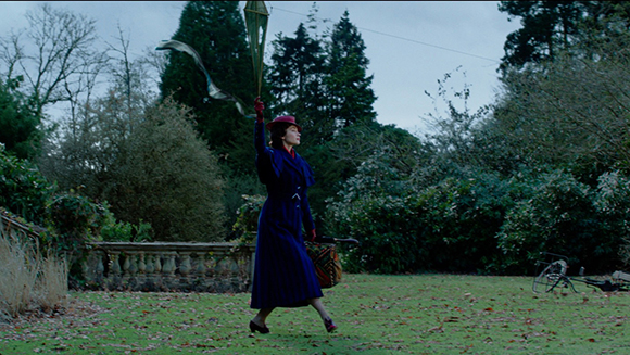 A woman in a long blue dress and red hat stands on a lawn holding a kite string.