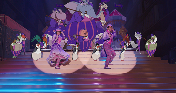 Performers dance on a lit stage in front of large purple animated animal backdrops.