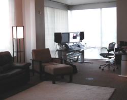 An office with a desk featuring dual monitors, a black office chair, and a brown armchair with an ottoman.