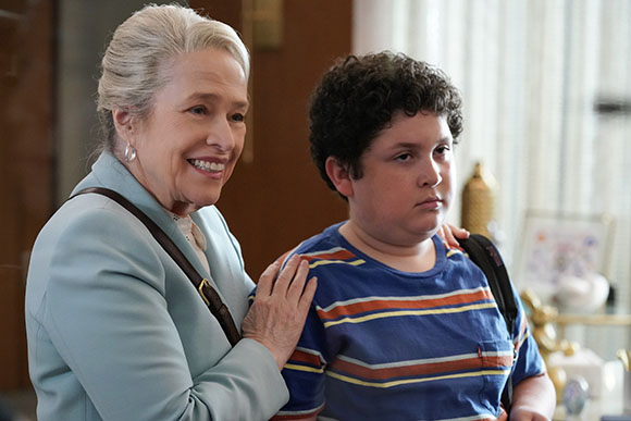 An older woman with white hair smiles at a young boy with curly hair wearing a striped shirt.