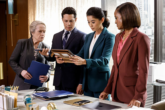 Four people in professional suits stand around a desk, focused on a small framed item held by a woman.