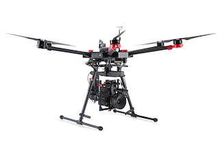 A large black multi-rotor drone with long arms and a professional camera mounted underneath on a white background.