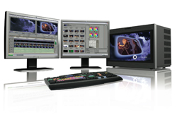 Dual monitors displaying video editing software, a computer tower, and a control panel on a reflective surface.
