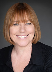 A smiling woman with reddish-brown hair and bangs wearing a black shirt.