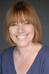 A smiling woman with shoulder-length reddish-brown hair and bangs wearing a blue shirt.