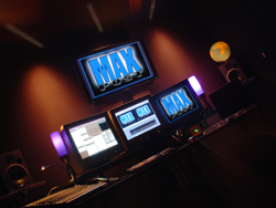 Three computer monitors on a desk in a dark room, displaying blue and white text on dark backgrounds.