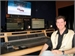 A man smiling while sitting in front of a large video editing console and multiple monitors.