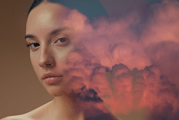 A portrait of a woman blended with swirling pink and purple clouds.