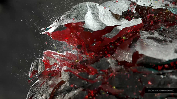 Dark, textured rock fragments exploding outward, revealing a vibrant red, crystalline interior against a dark background.