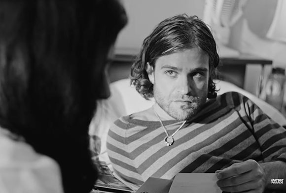 Black and white close-up of a man with wavy hair looking intently at a woman in the foreground.