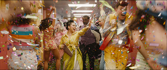 A group of people dancing and celebrating in a hallway as colorful confetti falls around them.