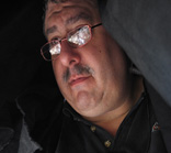 A man with dark hair, glasses, and a mustache looking slightly upward.