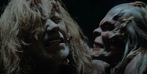 A person with long, messy hair grimaces while a pale, creature-like figure leans in close.