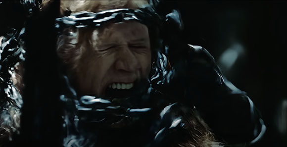 A person with a pained expression is tightly bound by thick, dark metal chains.