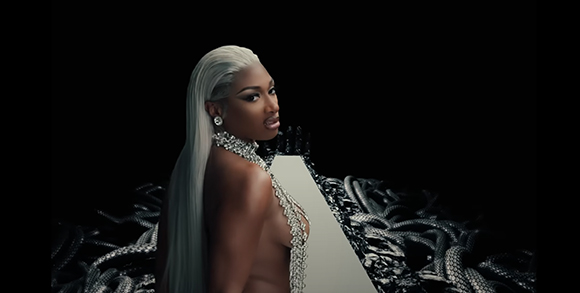 A woman with long platinum hair and silver jewelry poses against a dark background.