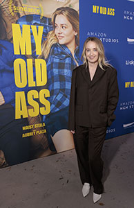 A woman in a dark brown suit standing in front of a My Old Ass movie poster.