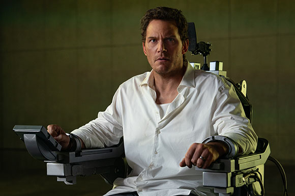 A man with short brown hair wearing a white button-down shirt sits in a large, metallic mechanical chair.