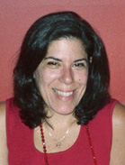 A smiling woman with shoulder-length dark hair wearing a red sleeveless top and a necklace.