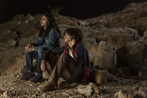Two men sit on large rocks in a dark, rocky landscape at night.
