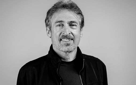 Black and white headshot of a middle-aged man with salt and pepper hair and a beard, smiling at the camera.