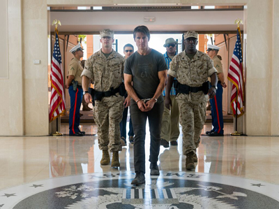 A man in a grey t-shirt and handcuffs walks between two Marines in desert camouflage.