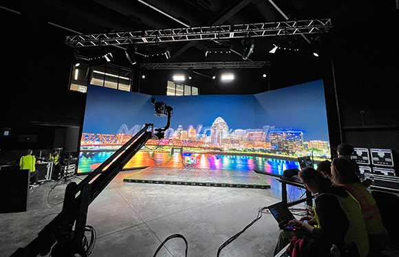 Film crew operating a camera crane in front of a large LED screen displaying a city skyline at night.