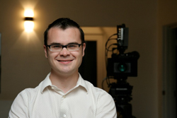A smiling man with dark hair and glasses wearing a white button-down shirt.