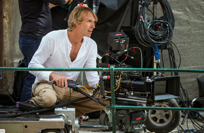 A man in a white shirt sits behind a professional film camera on a production set.