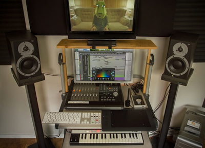 A computer monitor, studio monitors, a mixing console, and a MIDI keyboard on a desk.