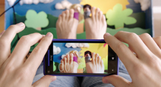 Hands holding a smartphone capturing a photo of feet decorated with small figures against a paper backdrop.