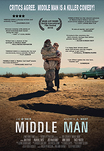 A man in a suit carries a person wrapped in a blanket through a desert landscape.
