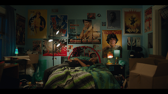 A person lies in bed in a dimly lit room decorated with numerous martial arts movie posters.