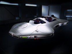 A sleek, silver aerodynamic concept vehicle with an open cockpit in a dark, minimalist room.
