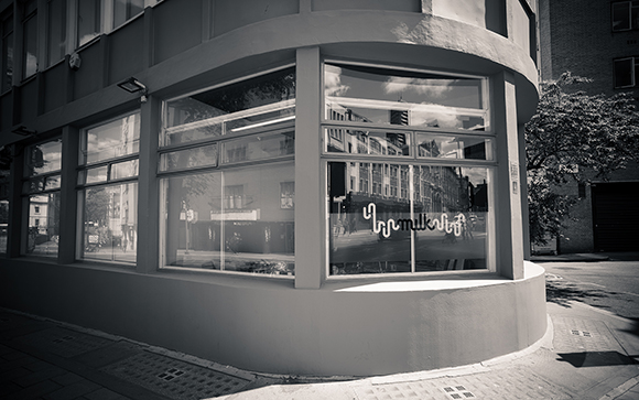 A black and white view of a curved building corner with large storefront windows reflecting the street.