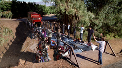 A large group of people standing along a long line of belongings laid out on the ground near a red truck.