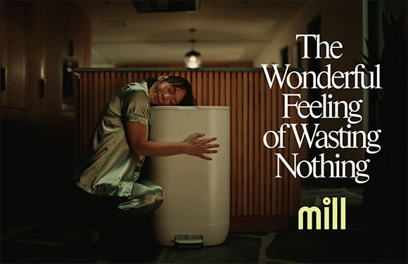 A person in light green pajamas kneels and hugs a white Mill kitchen appliance in a dimly lit room.