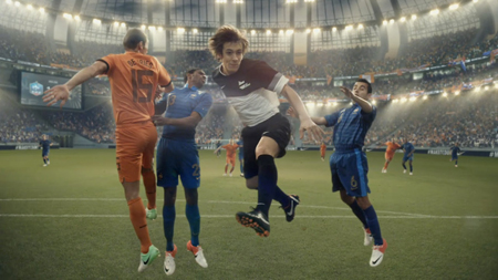 Soccer players in various colored jerseys jump and run on a field during a match in a crowded stadium.