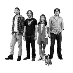 Black and white studio portrait of four adults and a small dog standing against a white background.