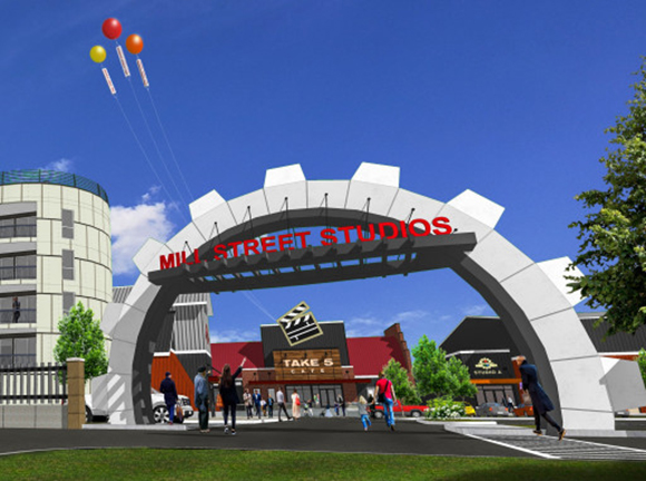 A large white gear-shaped archway with red text reading Mill Street Studios over a street scene.