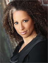 A woman with voluminous curly brown hair looks toward the camera against a blurred background.